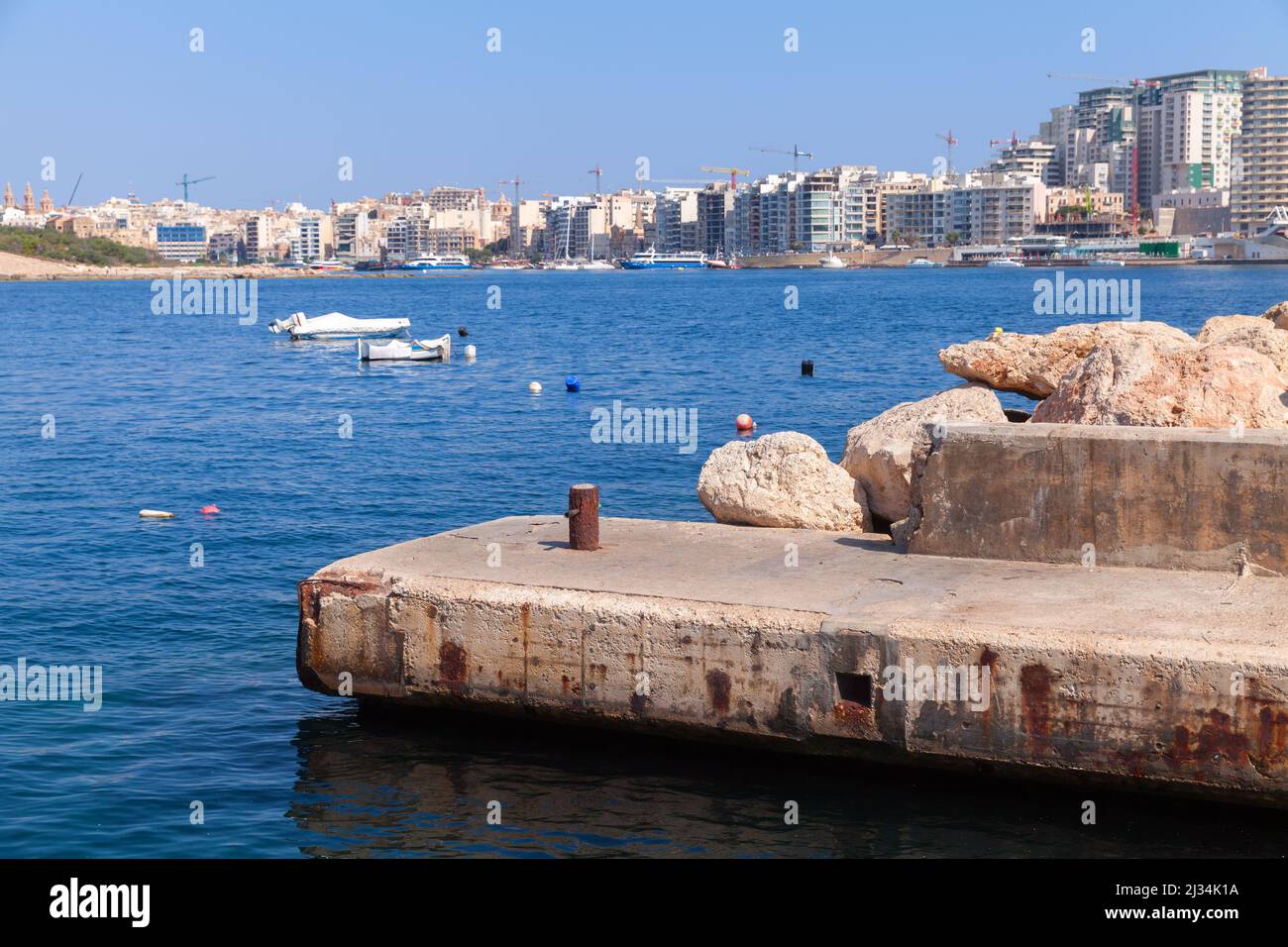 Vecchio molo di cemento vuoto. Case e barche moderne su uno sfondo. Vista sul mare di Sliema, Malta Foto Stock