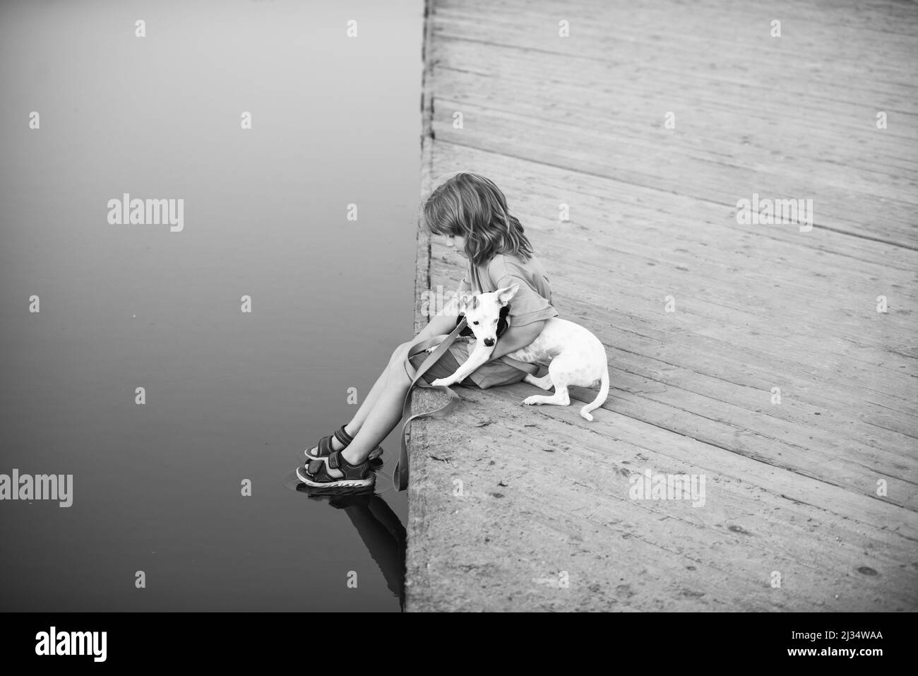 Bambino piccolo con cane seduto in parco vicino all'acqua. Foto Stock