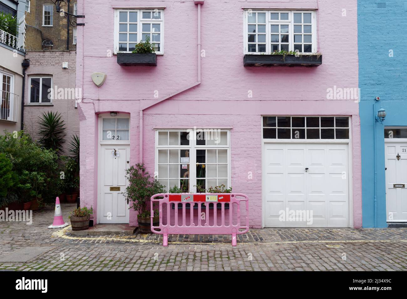 Londra, Grande Londra, Inghilterra, marzo 29 2022: Case di mews rosa e blu con un cono di traffico rosa e barriera Foto Stock