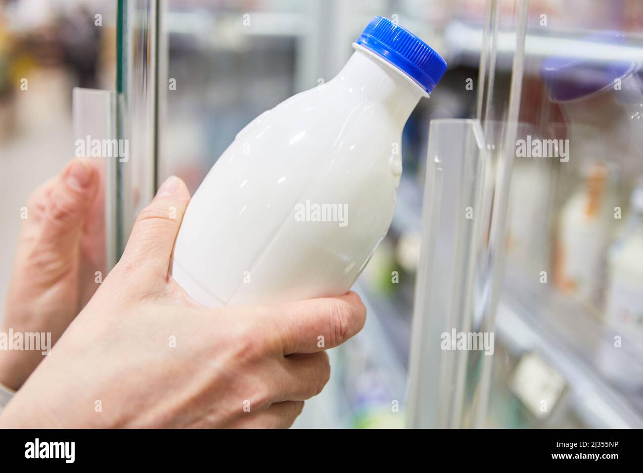 Mano che tiene una bottiglia con latte vegano o sostituto del latte sul ripiano refrigerato nel supermercato Foto Stock