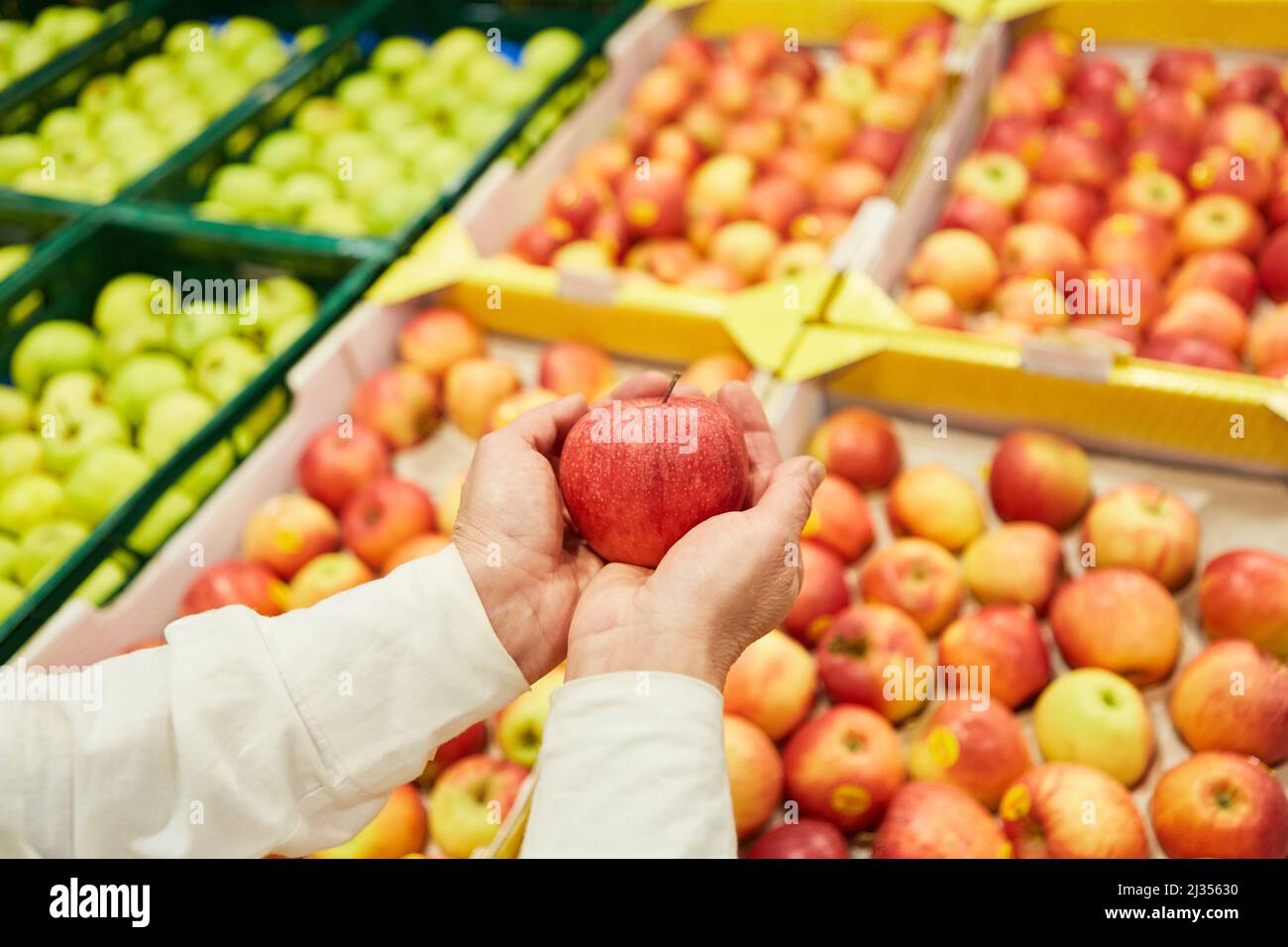 Le mani di un cliente tengono una mela mentre acquistano nel mercato o nel supermercato Foto Stock