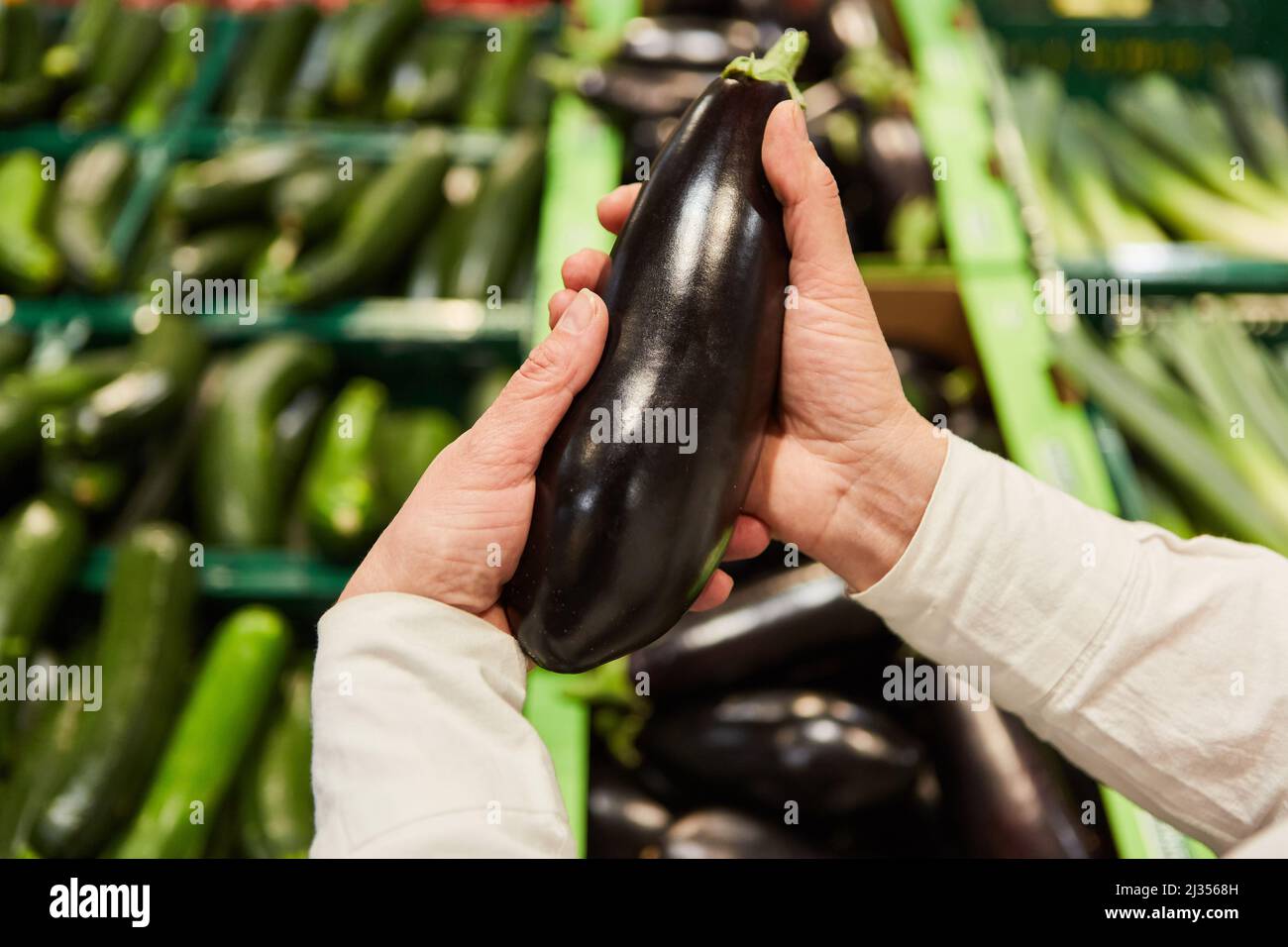 Le mani di un cliente detengono una melanzana mentre acquistano nel supermercato o nel mercato settimanale Foto Stock
