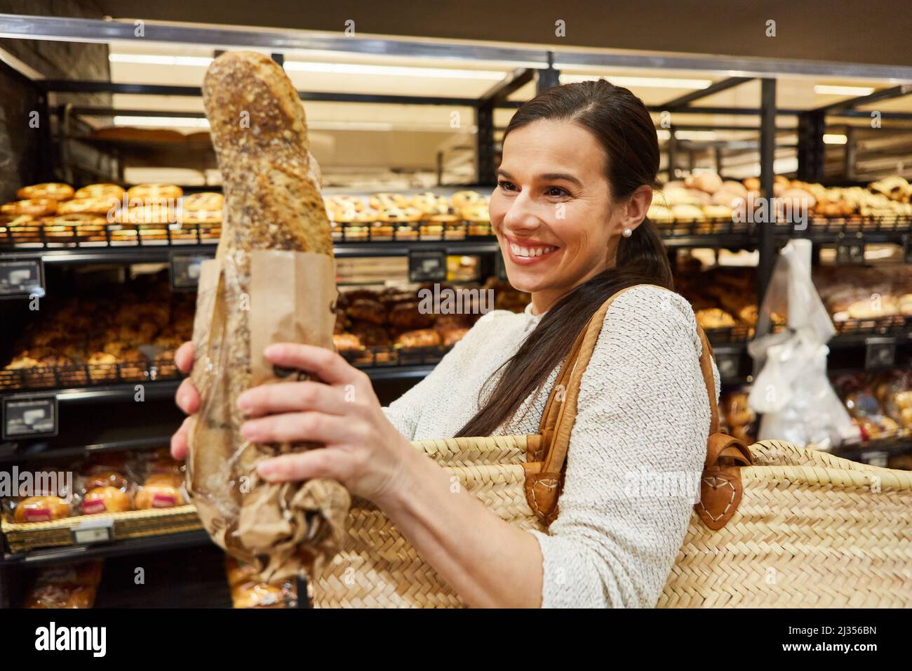Giovane donna con shopping bag acquista un pane fresco baguette in panetteria al supermercato Foto Stock Giovane donna con shopping bag acquista un pane fresco baguette in panetteria al supermercato Foto Stock