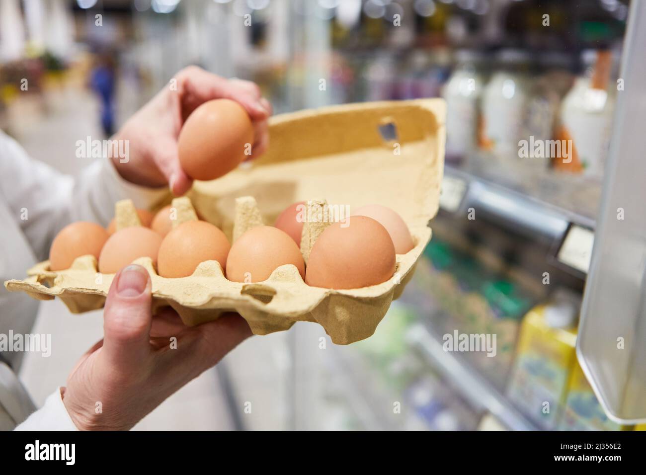 Mano di un cliente che tiene un cartone di uova fresche biologiche mentre acquista al supermercato Foto Stock