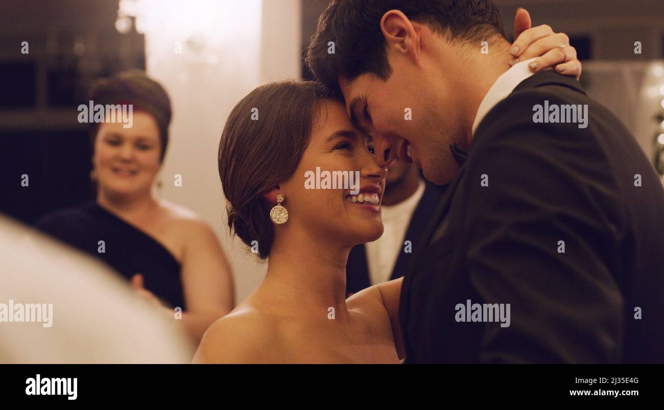È così perfetto. Scatto corto di una giovane coppia affettuosa sposata che balla lentamente con i loro ospiti in background al loro ricevimento di nozze. Foto Stock