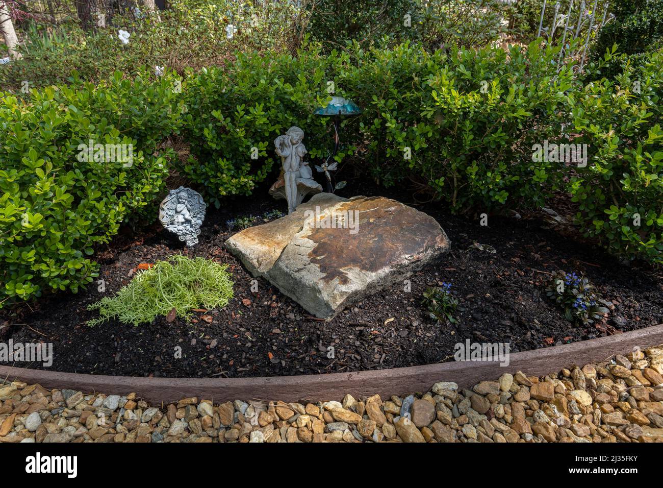 Piccola casa giardino caratteristica con una grande roccia, coperta di terra e una siepe di legno di bosso. Foto Stock
