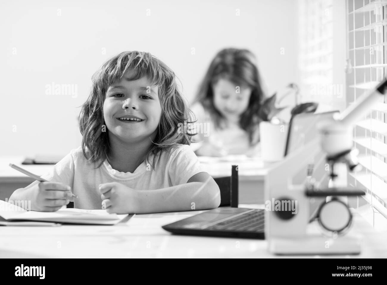 Ragazzo di scuola seduto al tavolo, scrivendo i compiti o preparandosi per l'esame. Felice sorridente bambino studio. Poco apprendimento ostinato. Foto Stock