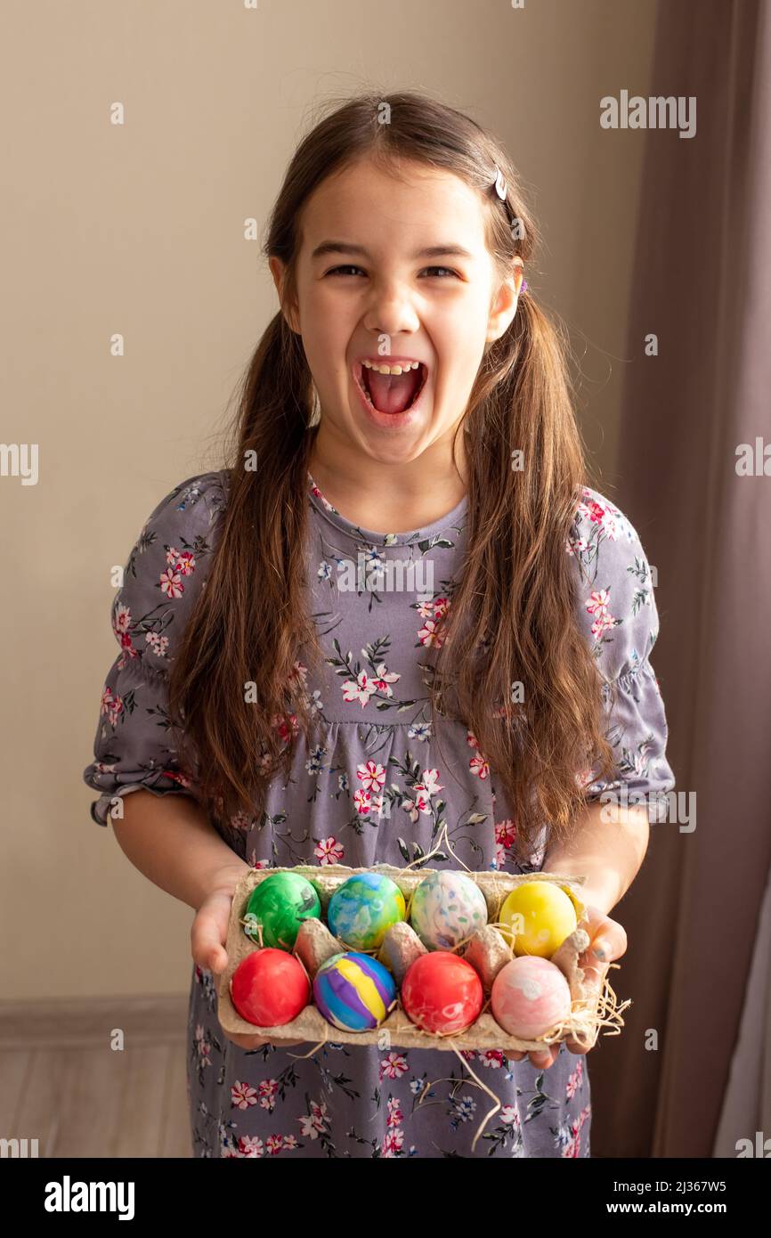 Una ragazza piccola e divertente bruna in abito tiene un vassoio di cartone con uova colorate Foto Stock