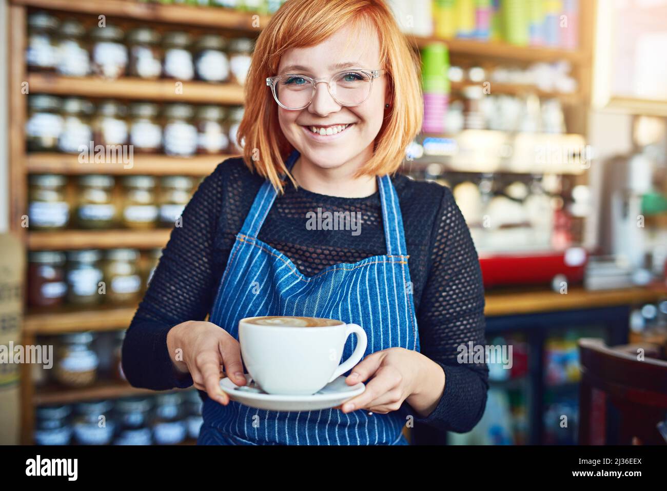 Combinando il suo amore per il caffè con il suo spirito imprenditoriale. Shot corto di una donna che serve il caffè in una caffetteria. Foto Stock