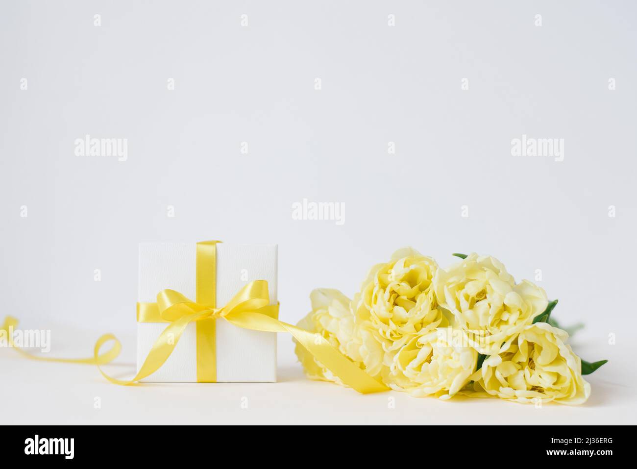 Primavera composizione di un bouquet di tulipani gialli, un regalo con un arco giallo e nastro su sfondo bianco. Primavera, giorno delle donne, giorno della mamma, compleanno. Foto Stock