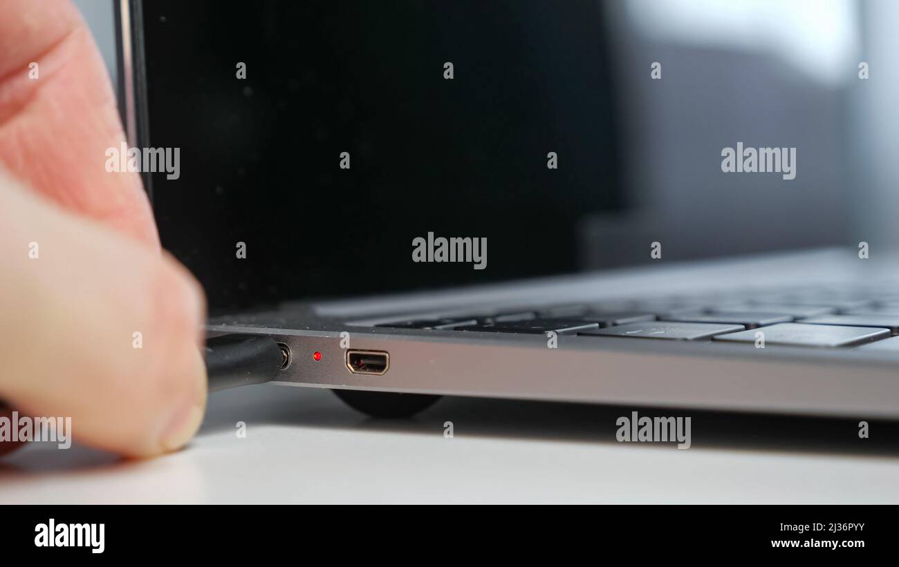 Man collega il caricabatteria al computer con la batteria scarica in ufficio Foto Stock