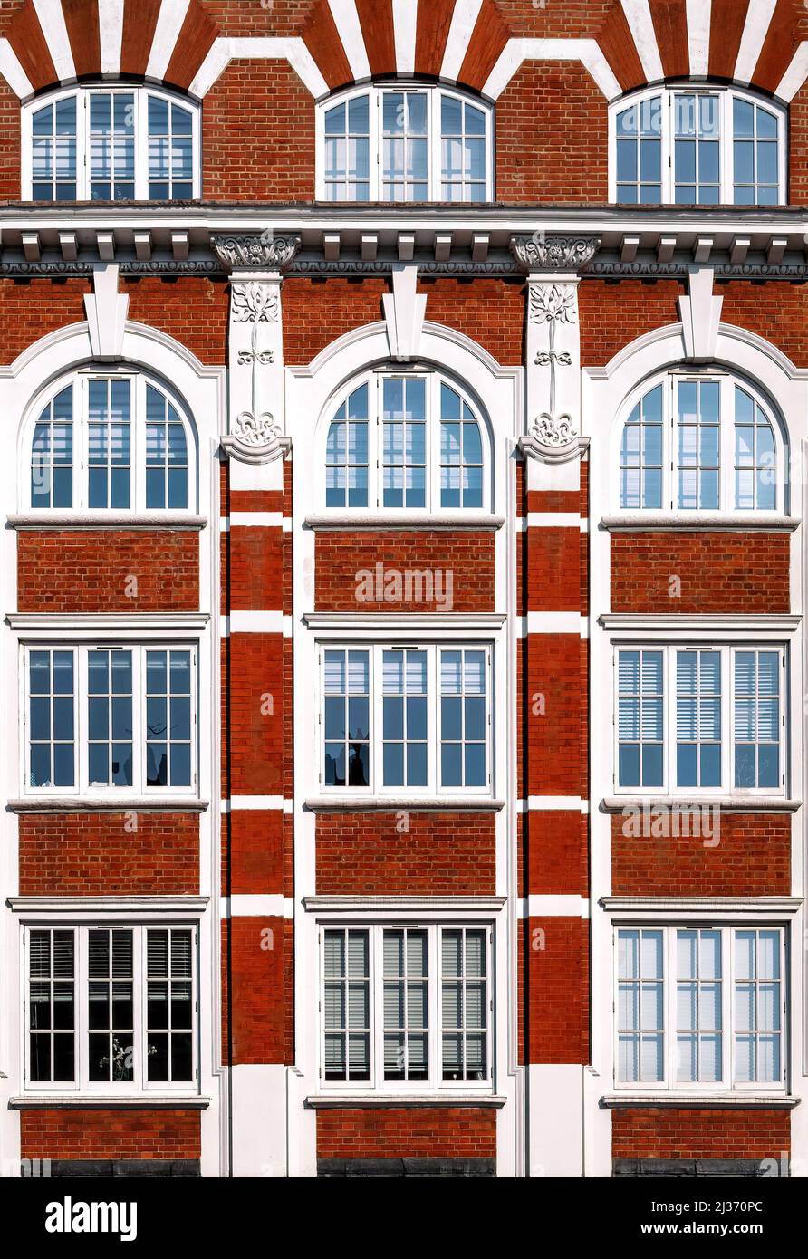 Dettaglio architettonico di un edificio vittoriano, con mattoni rossi, finestre ad arco e intonaci decorativi in stile Art Nouveau. Imag. Sfondo geometrico Foto Stock