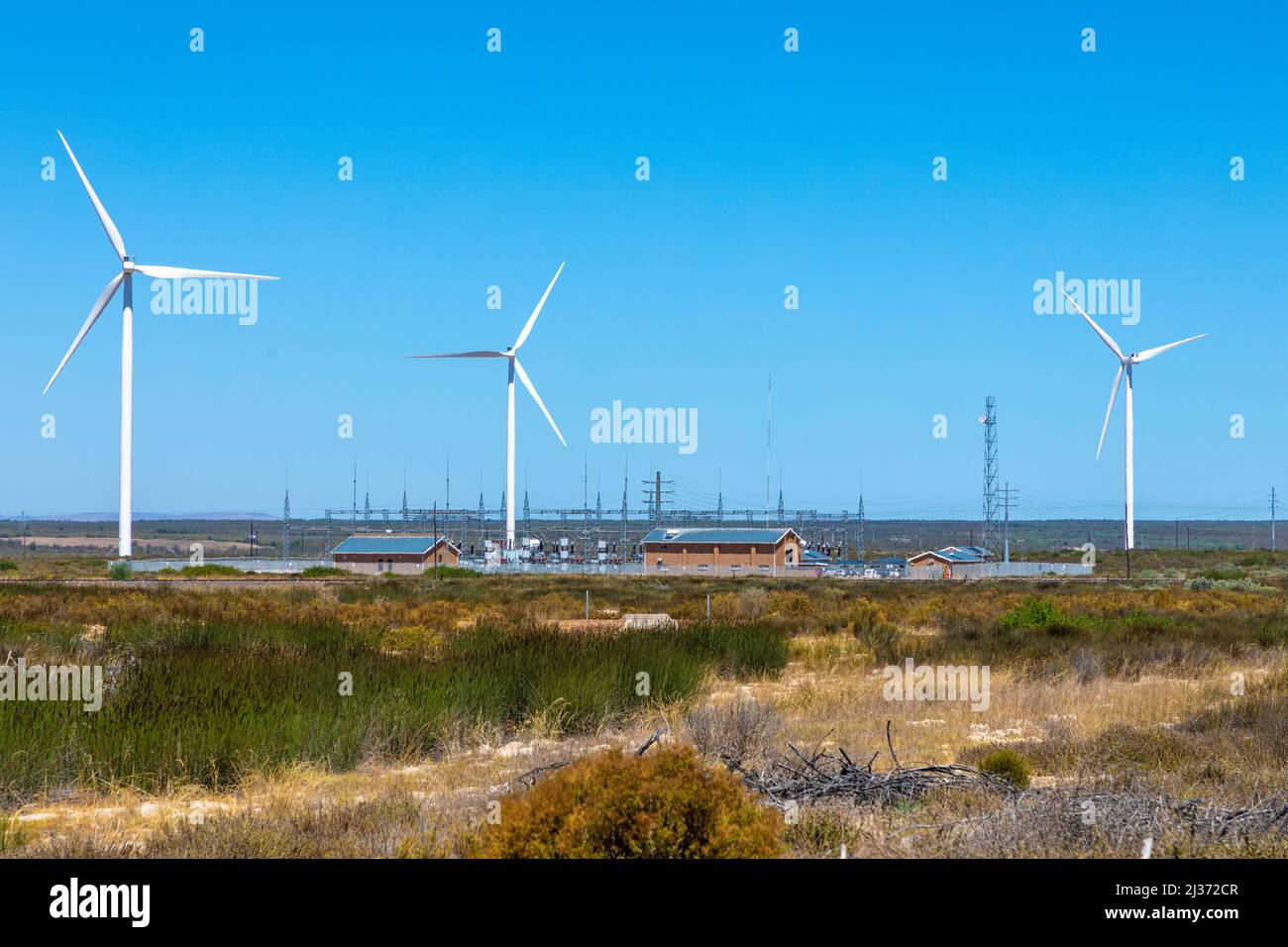Fattoria di turbine eoliche con edificio di scambio elettrico, in un'area semi-desertica in una calda giornata estiva. Foto Stock