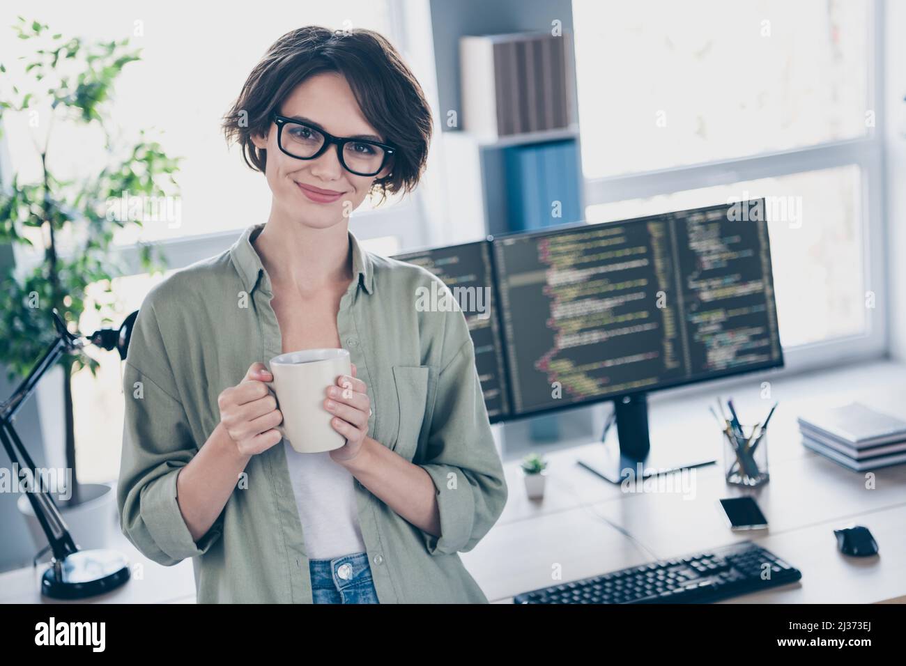 Ritratto di attraente sicuro cheery ragazza hacker supporto tecnico top manager senior bere caffè al posto di lavoro stazione al chiuso Foto Stock