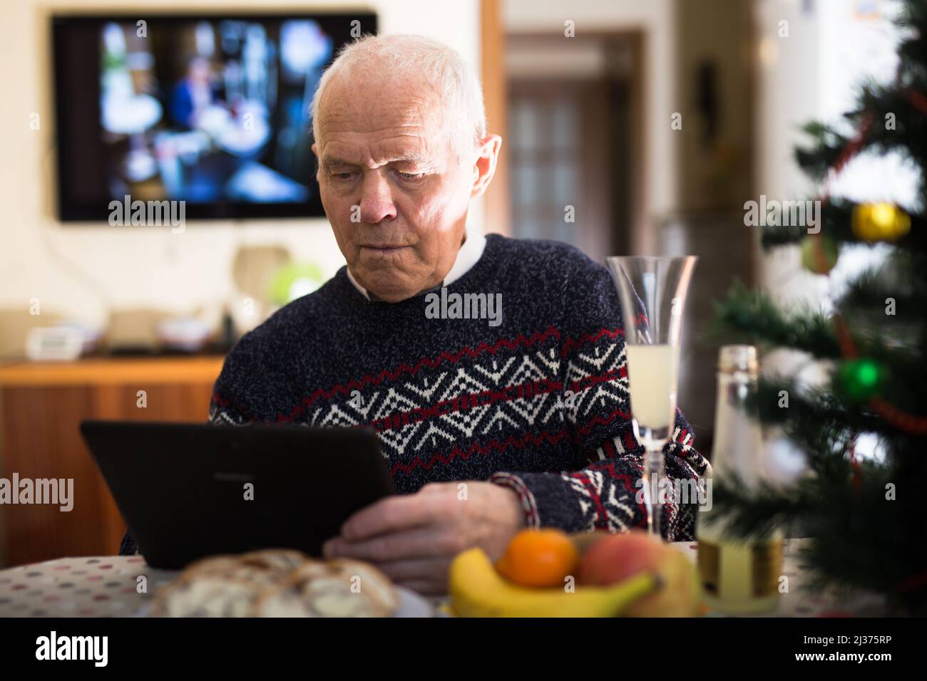 Ederly uomo seduto al tavolo di casa con tavoletta durante la celebrazione di Capodanno Foto Stock