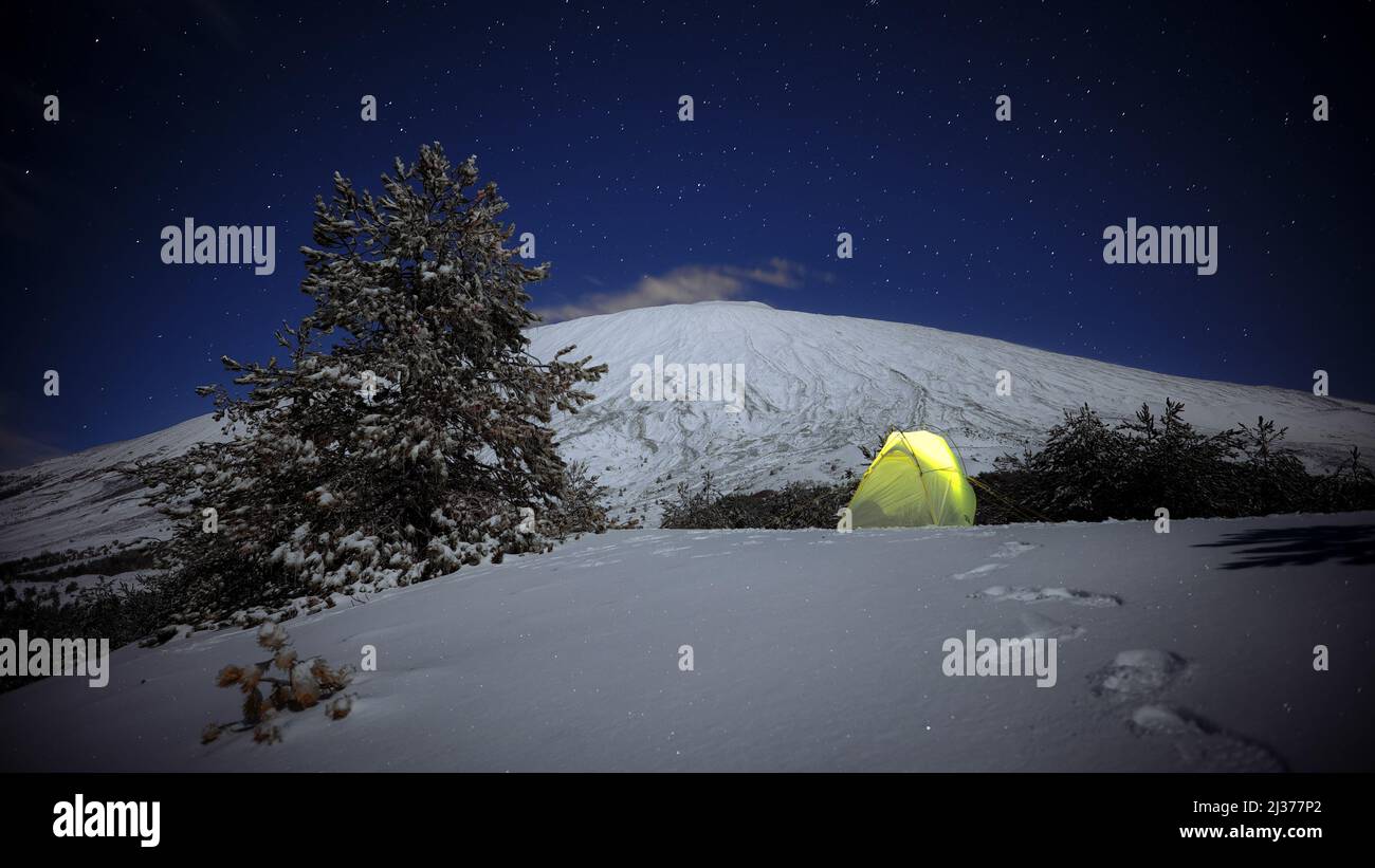 Stelle notturne sulla tenda gialla illuminata sulla neve e sul Monte Etna, Sicilia Foto Stock