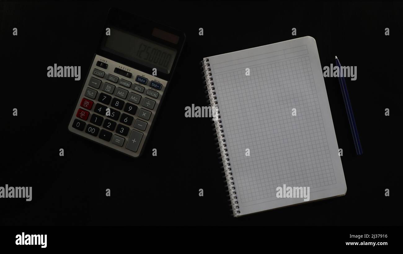 Concept tavolo nero con calcolatrice e notebook, contabilità con penna e vuoto, calcolo, isolato su sfondo nero, vista dall'alto Foto Stock