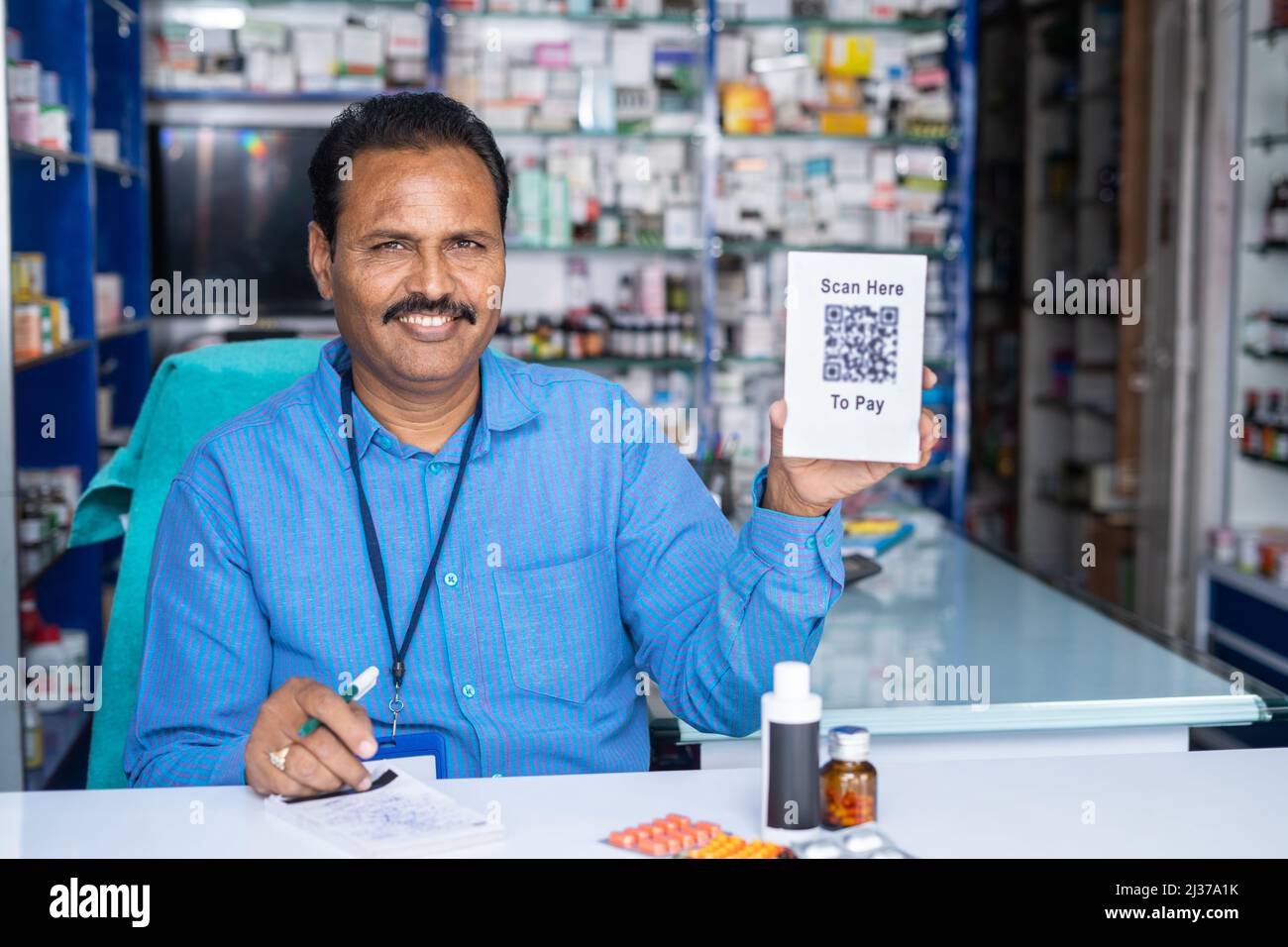 happy farmacista mostrando scansione qui per pagare qr codice segno bordo per l'acquisto guardando fotocamera al negozio medico al dettaglio - concetto di pagamento senza contanti Foto Stock