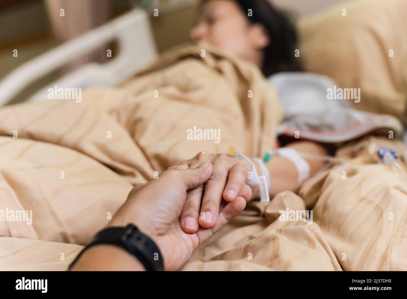 Mano del marito che tiene la mano della moglie sul letto nella stanza dell'ospedale. Foto Stock