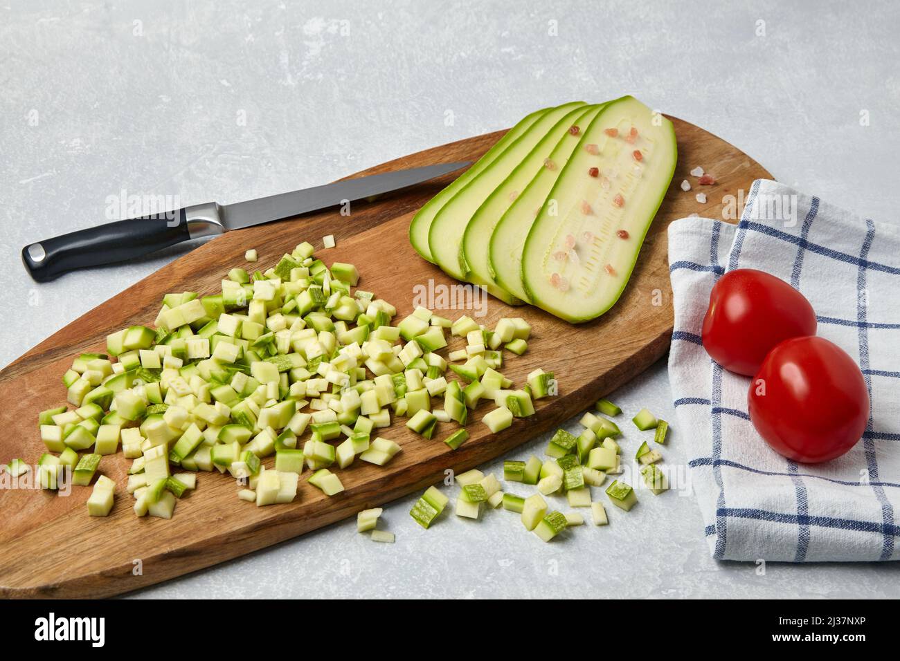 Verdure a fette di zucchine su un tagliere di legno e pomodori su un tavolo leggero in cemento. Foto Stock