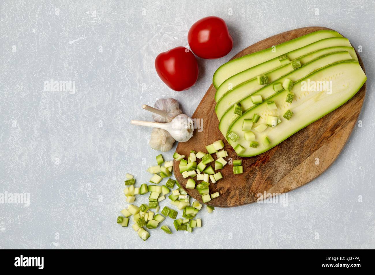 Verdure a fette con zucchine su un tagliere di legno, pomodori e aglio su un tavolo in cemento leggero. Vista dall'alto con spazio di copia. Disposizione piatta Foto Stock