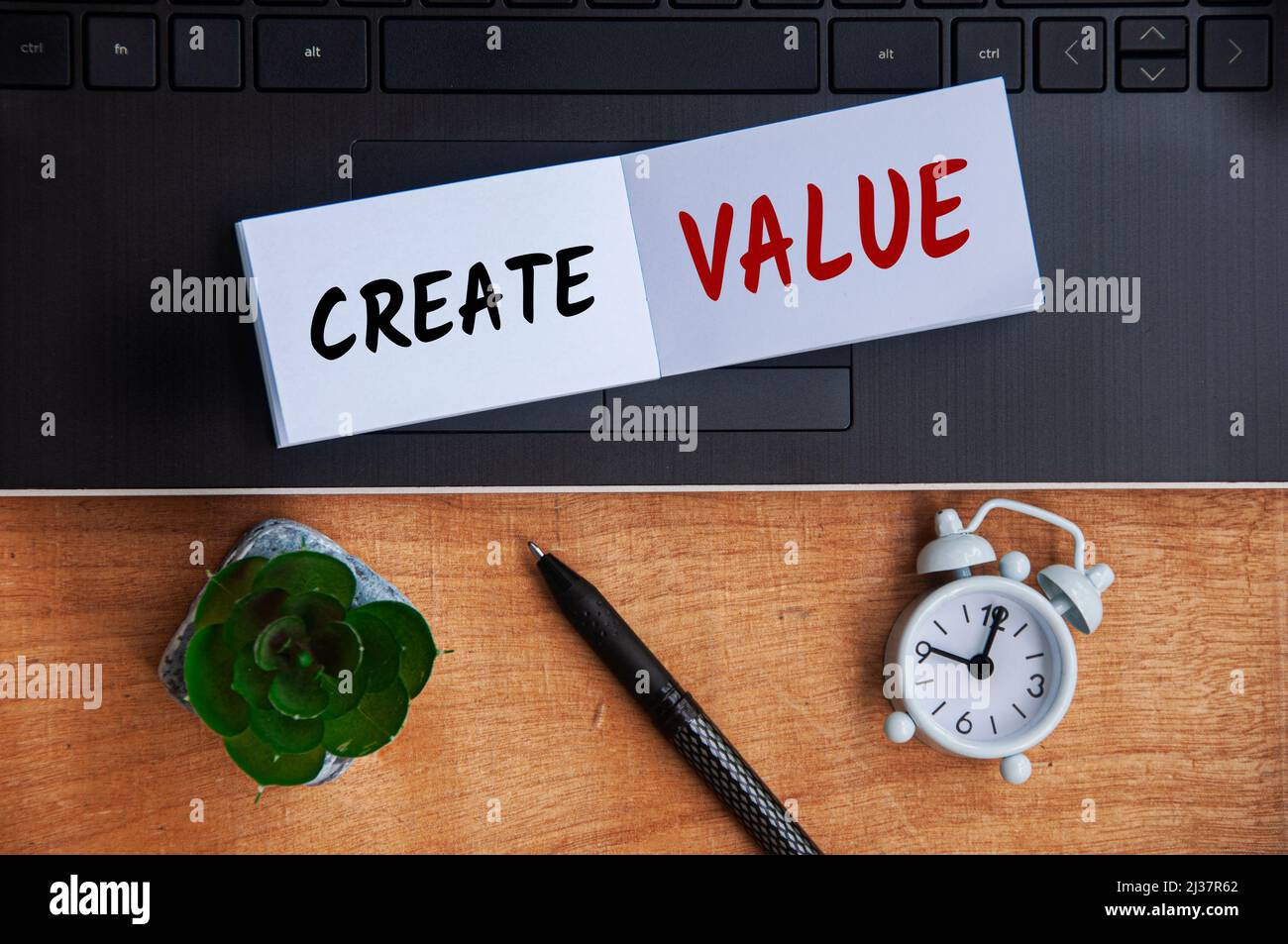 Crea testo di valore su blocco note con laptop, orologio, penna e sfondo in legno. Foto Stock