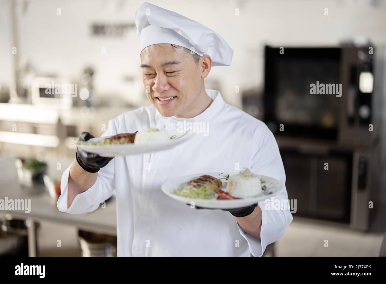 Ritratto di giovane felice bello chef sorridente in uniforme in piedi con pasto pronto in cucina. Buon cucina asiatica che lavora al ristorante. Concetto di occupazione professionale e alta cucina Foto Stock