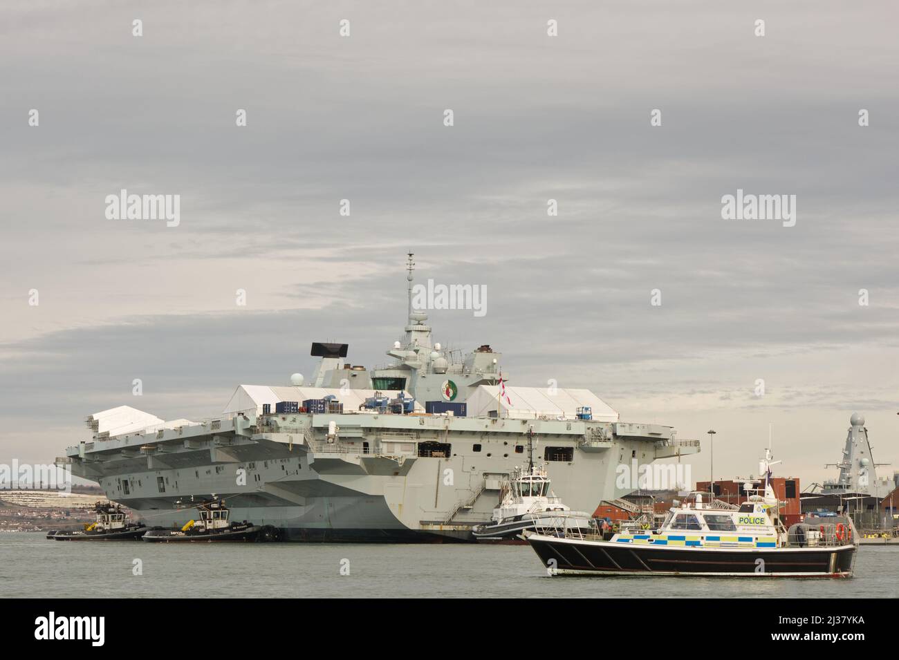 La Royal Navy Aircraft Carrier Queen Elizabeth ormeggiata nel cantiere navale di Portsmouth, Hampshire, Inghilterra. Con pattugliamento della polizia lancio sul servizio di guardia. Visualizzato da Foto Stock