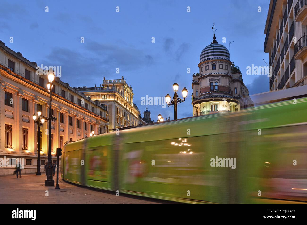 Tram che passa attraverso Avenida de la Constitución al crepuscolo con l'edificio la Adriatica a Siviglia Andalusia Spagna. Foto Stock