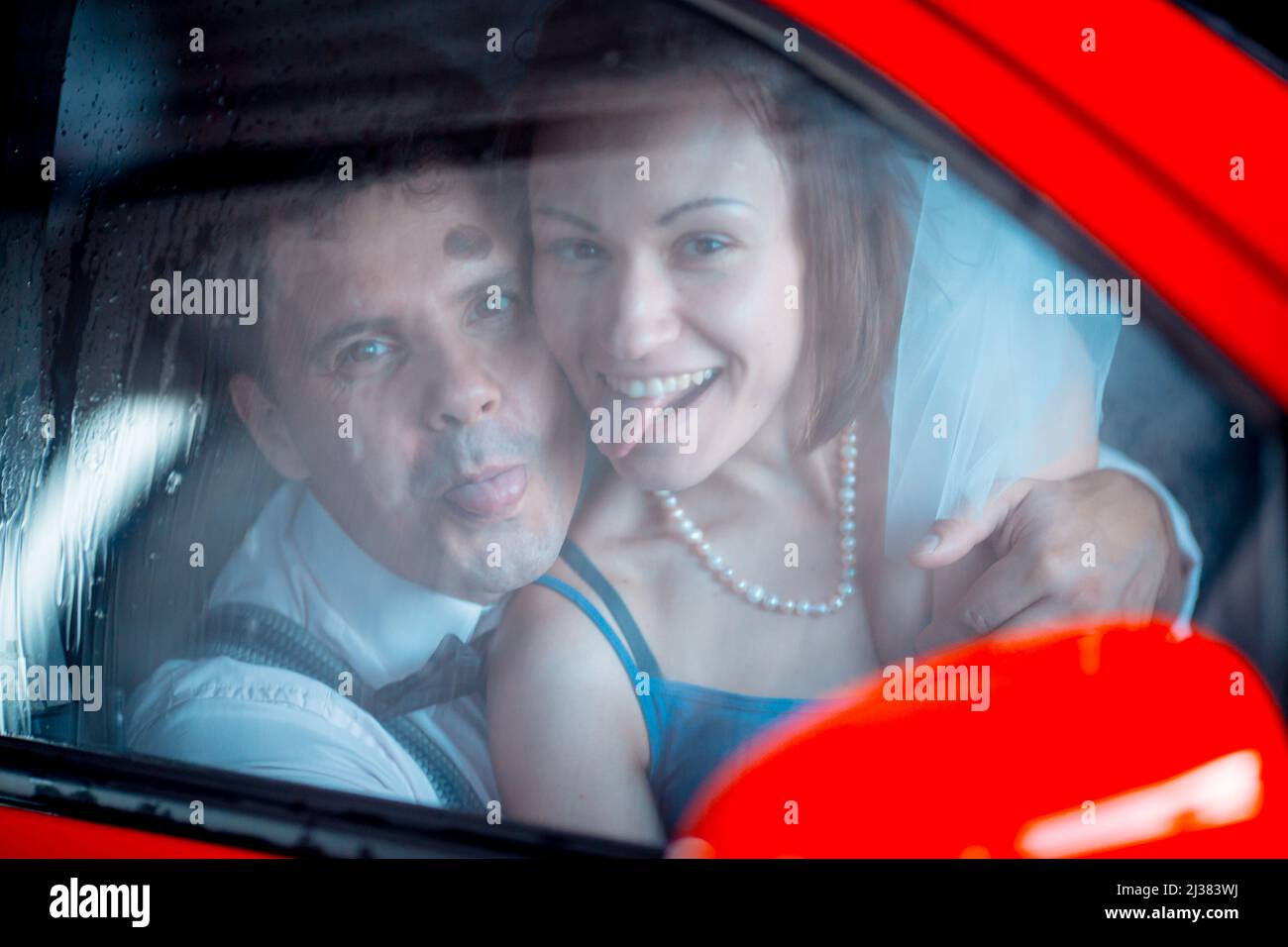 Ritratto di una giovane coppia in abito da sposa che celebra il loro anniversario di matrimonio. La coppia sta lavando la macchina. Sorridi, bacia, amore. Foto Stock