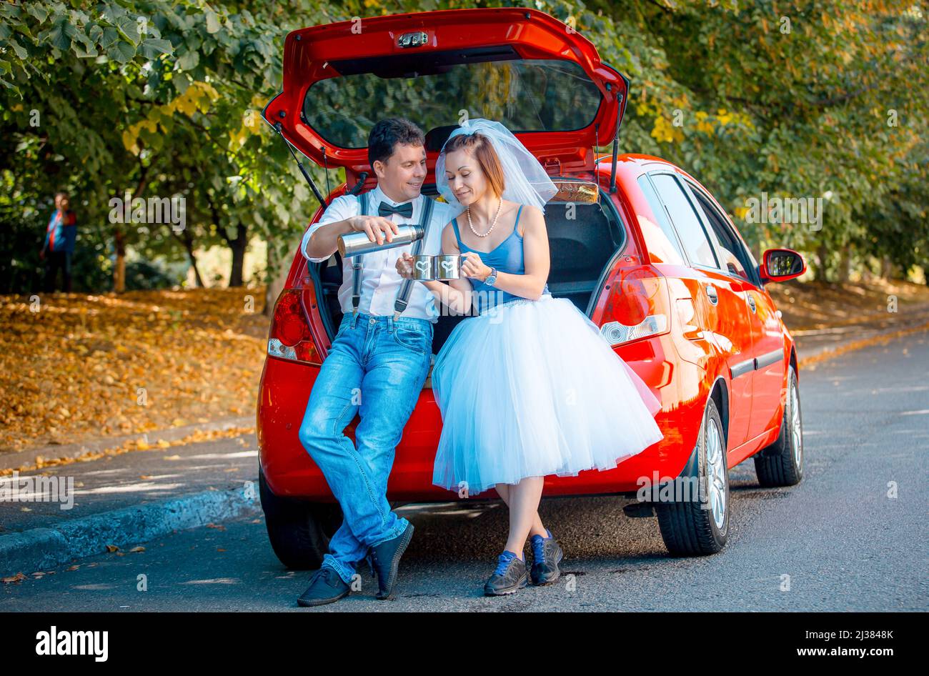 Ritratto di una giovane coppia in abito da sposa che celebra il loro anniversario di matrimonio. La coppia sta lavando la macchina. Sorridi, bacia, amore. Foto Stock