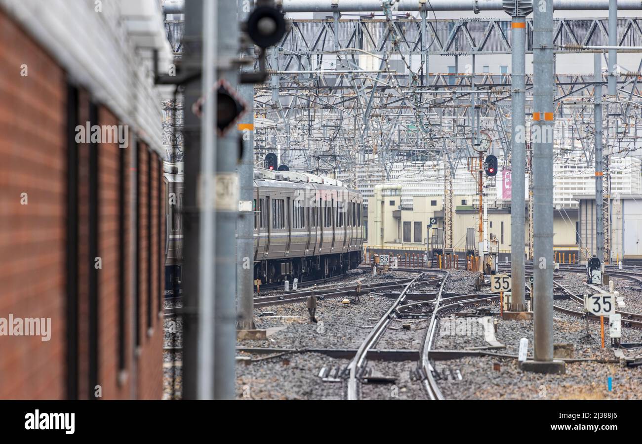 Il treno lascia la stazione oltre le rotaie vuote e la massa del cablaggio sospeso Foto Stock