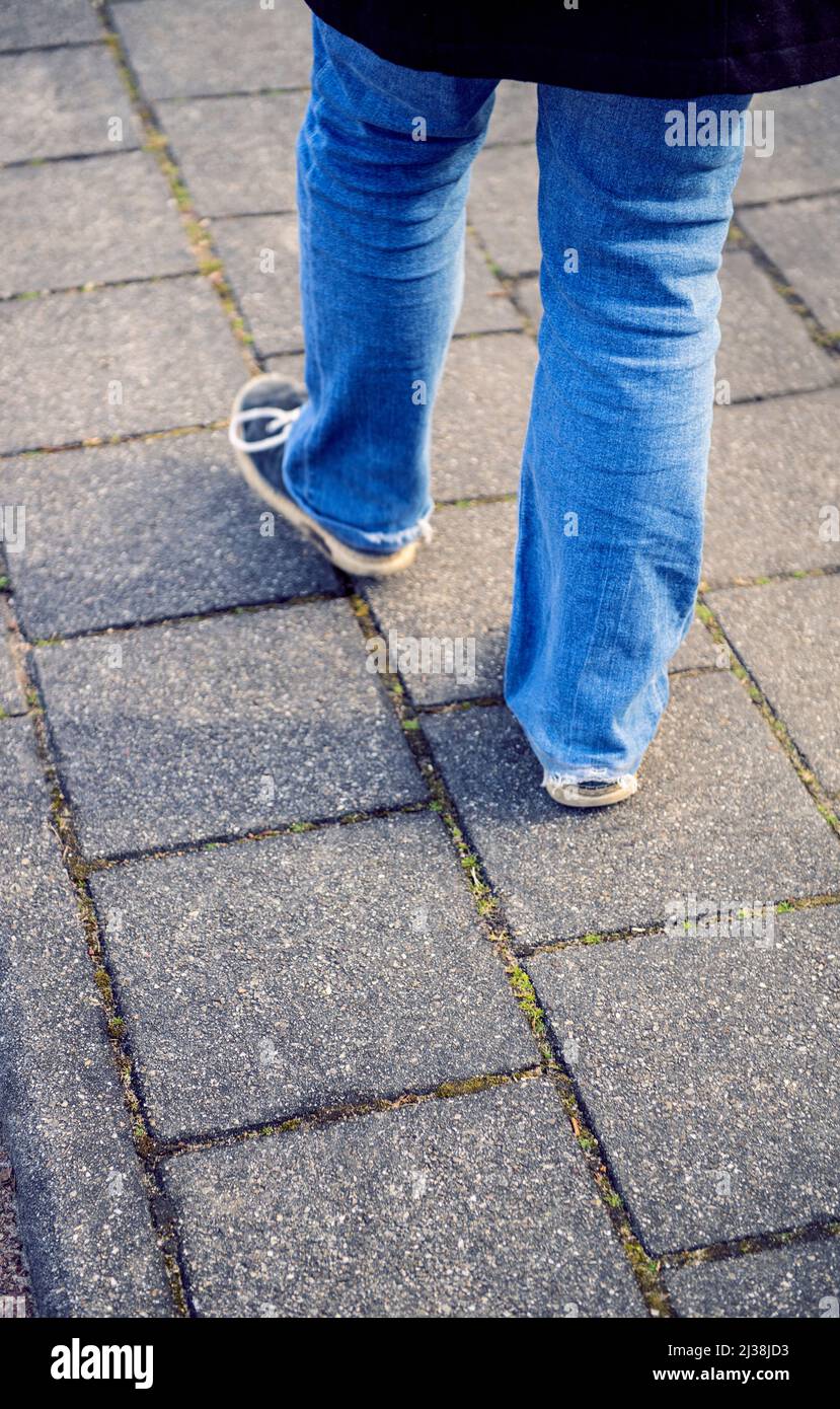 Gambe di una giovane donna che indossa jeans, che cammina su un marciapiede Foto Stock