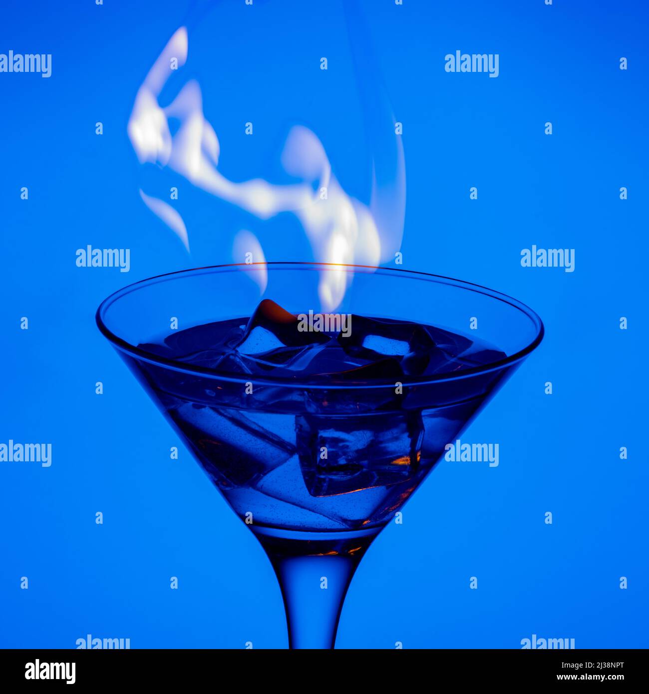 Bevanda alcolica bruciante con cubetti di ghiaccio, su sfondo blu a gradiente, cornice verticale. Cocktail bruciante al tavolo in un bar. Bevanda alcolica blu e. Foto Stock