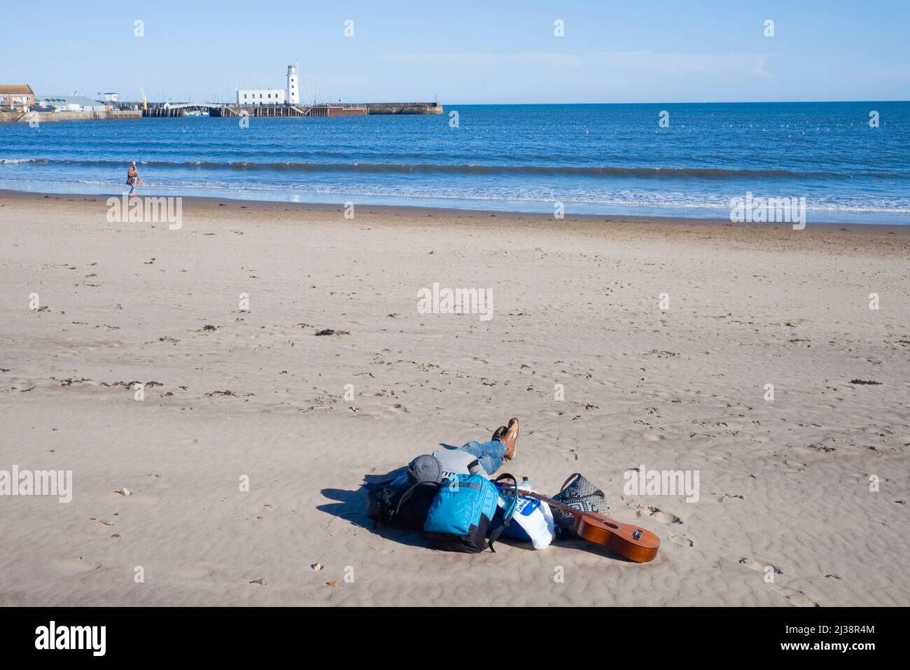Un uomo che dorme sulla spiaggia di Scarborough con borse e una chitarra Foto Stock