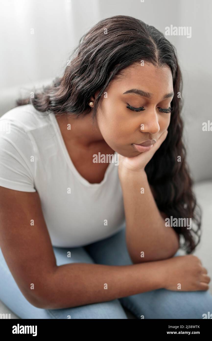 Stressata miserabile donna nera soffre di dolore problema, depressa solitario sconvolto ragazza africana piangendo da solo sul divano Foto Stock