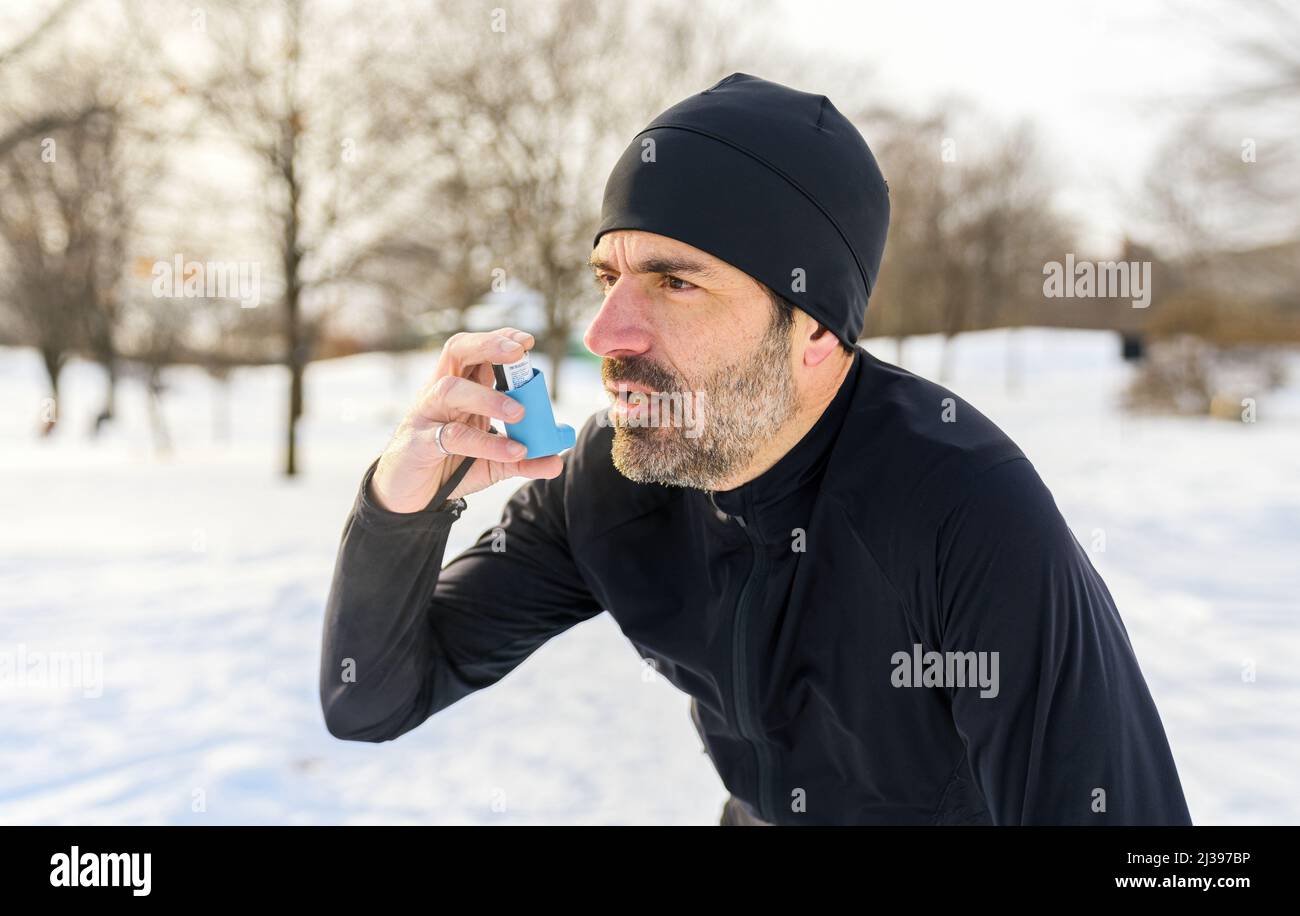 l'uomo maturo che corre in inverno nel parco ha alcune difficoltà respiratorie e usando la pompa dell'asma Foto Stock