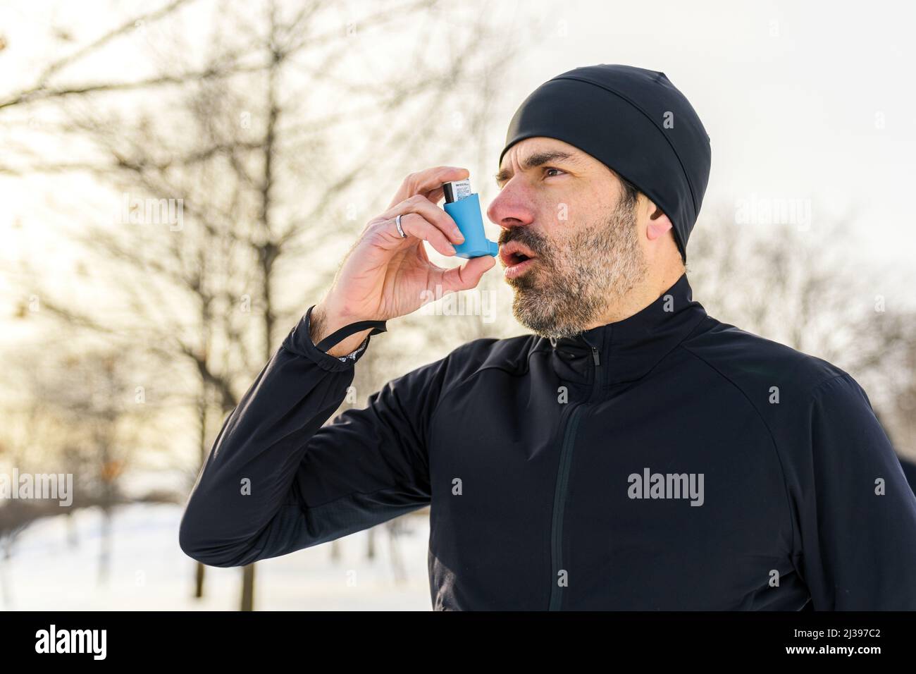 l'uomo maturo che corre in inverno nel parco ha alcune difficoltà respiratorie e usando la pompa dell'asma Foto Stock