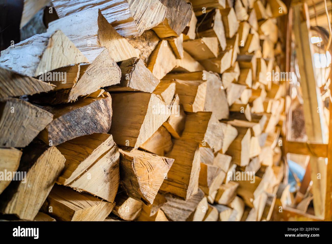 Legna da ardere tagliata e tagliata impilata e raccolta per l'inverno in un capannone da legna. Deposito legna da ardere in estate Foto Stock