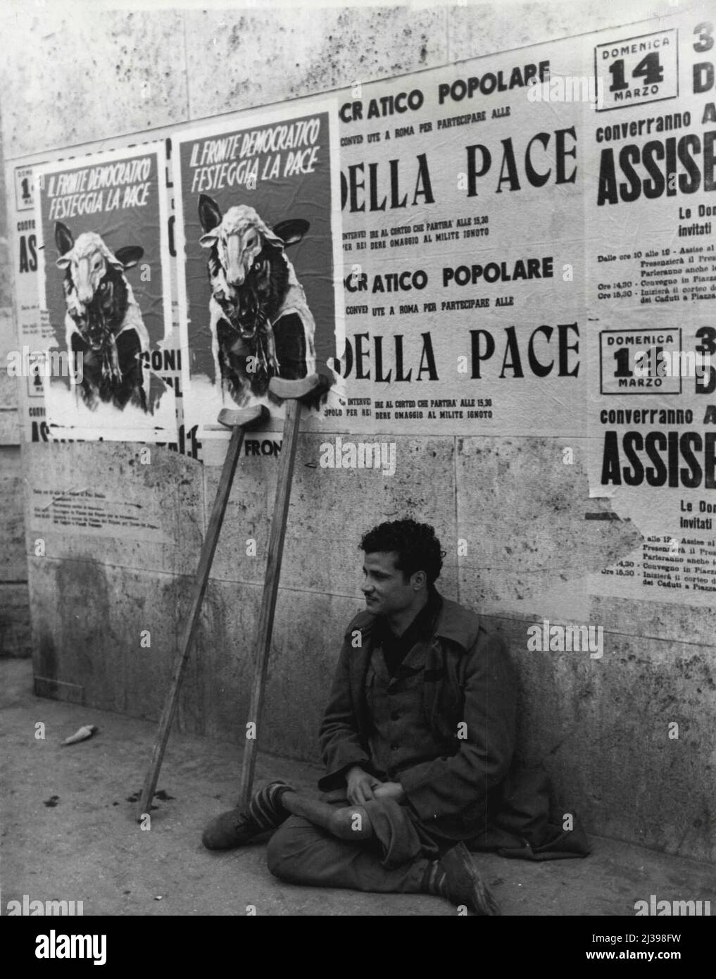 Poster delle elezioni italiane: Un mendicatore siede sotto i poster dei  democratici cristiani su un muro di Roma. I poster mostrano un lupo in  abiti di pecora. Sopra il lupo è scritto "