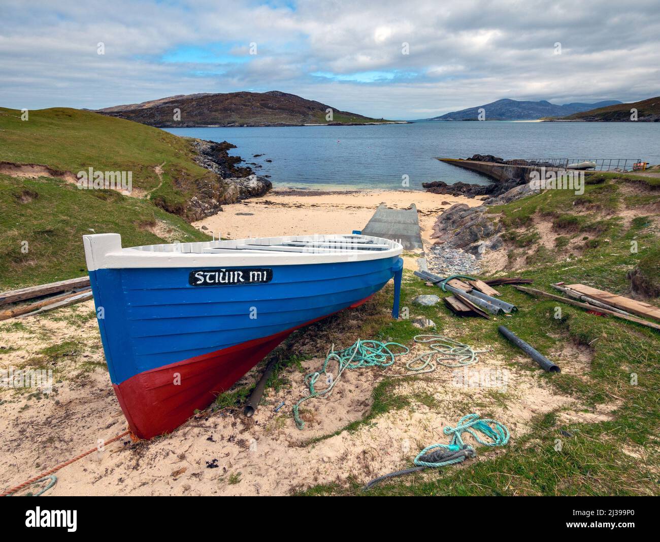 Barca di legno blu con scalo e molo a Port A' Tuath, Hushinish con Caolas An Scarp e Island of Scarp Beyond, Isola di Harris, Scozia, Regno Unito Foto Stock