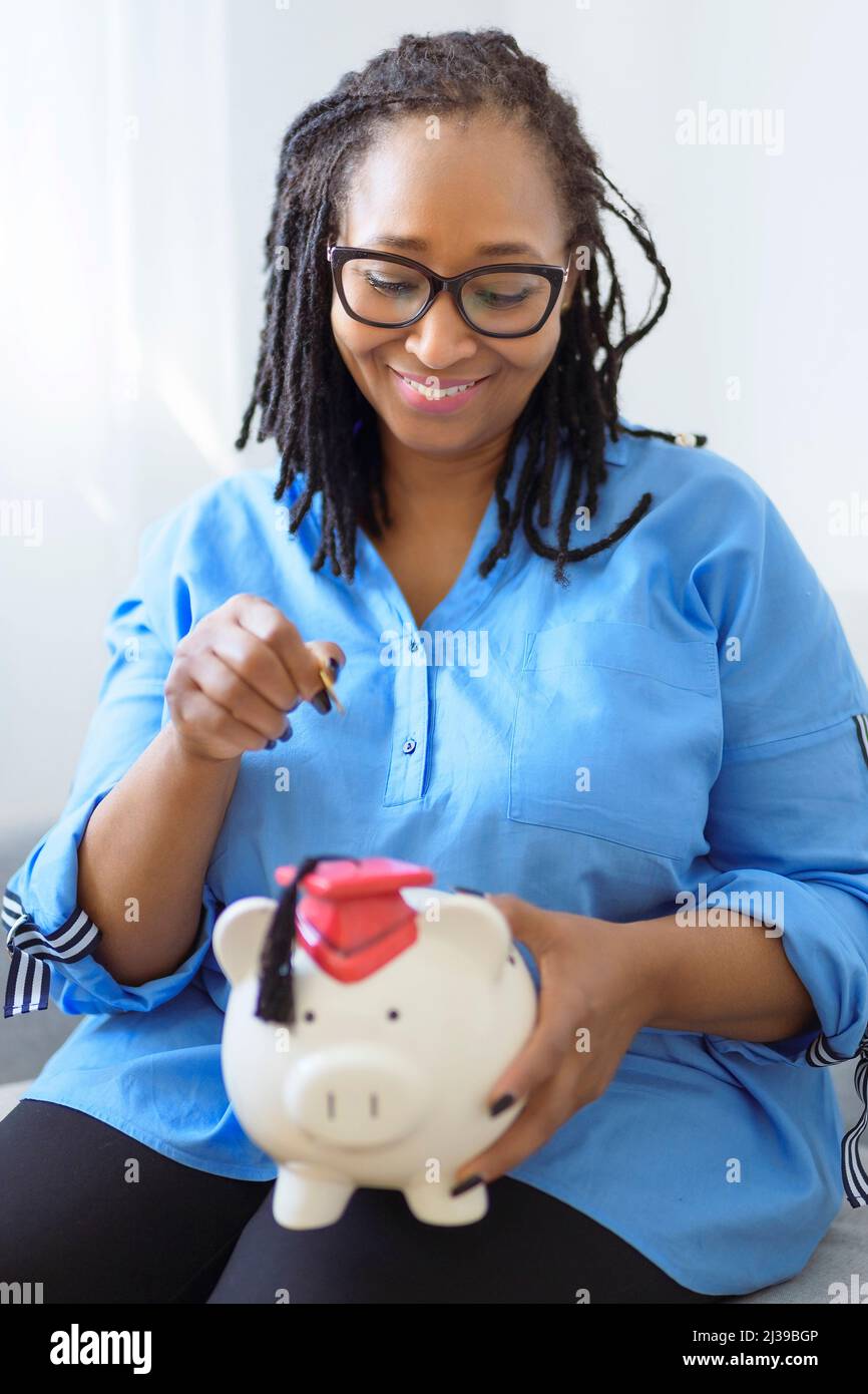 Bella donna nera tiene una banca rosa piggy che rappresenta il risparmio e la pensione Foto Stock