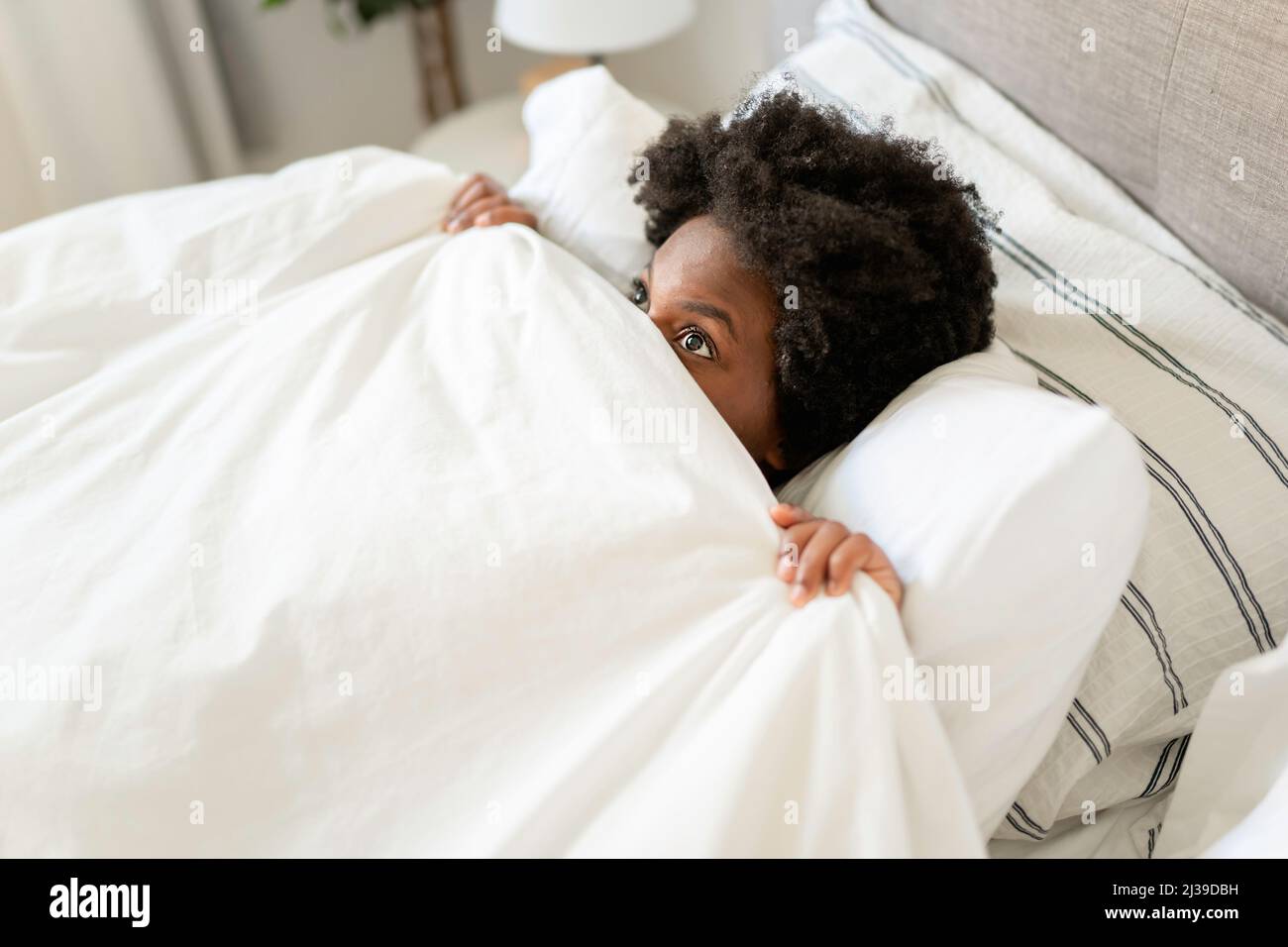 Bella giovane donna africana nella parte superiore del serbatoio che giace nella faccia di copertura del letto con foglio Foto Stock