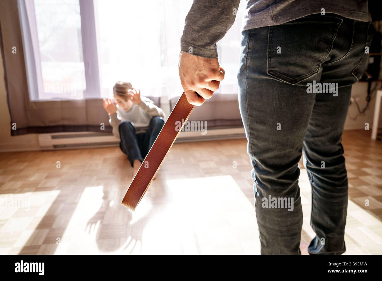 Ragazzo triste seduto sul pavimento con il padre davanti a lui con la cintura a portata di mano. Foto Stock