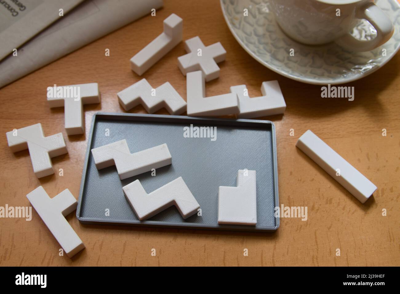 Vista dall'alto di un tavolo dove qualcuno sta cercando di risolvere un puzzle pentominoe accanto a una tazza di caffè e un giornale Foto Stock