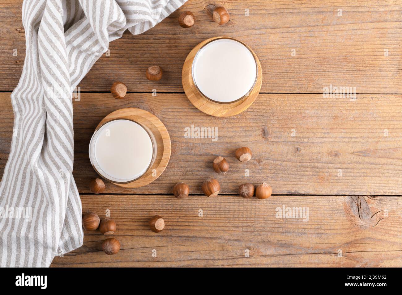 Latte di nocciola vegano non diario in vetro con nocciole intere su un tovagliolo di lino su un rustico sfondo di legno. La bevanda di nocciola priva di lattosio è la base vegetale Foto Stock