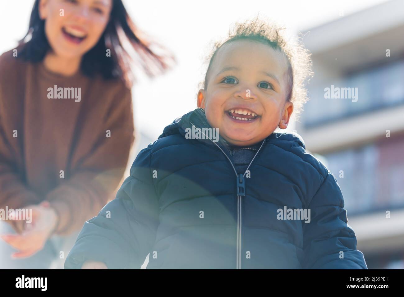 Divertito bella madre e il suo biraciale ridente ragazzo sorridente toddler correre nel quartiere, godendo bel tempo soleggiato. Foto di alta qualità Foto Stock
