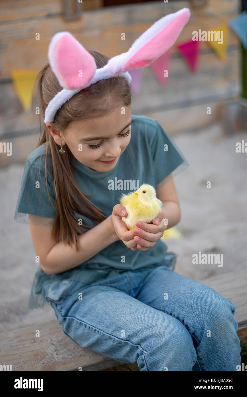 una ragazza carina in orecchie conigliate sta tenendo un pollo. Buona Pasqua. Foto Stock