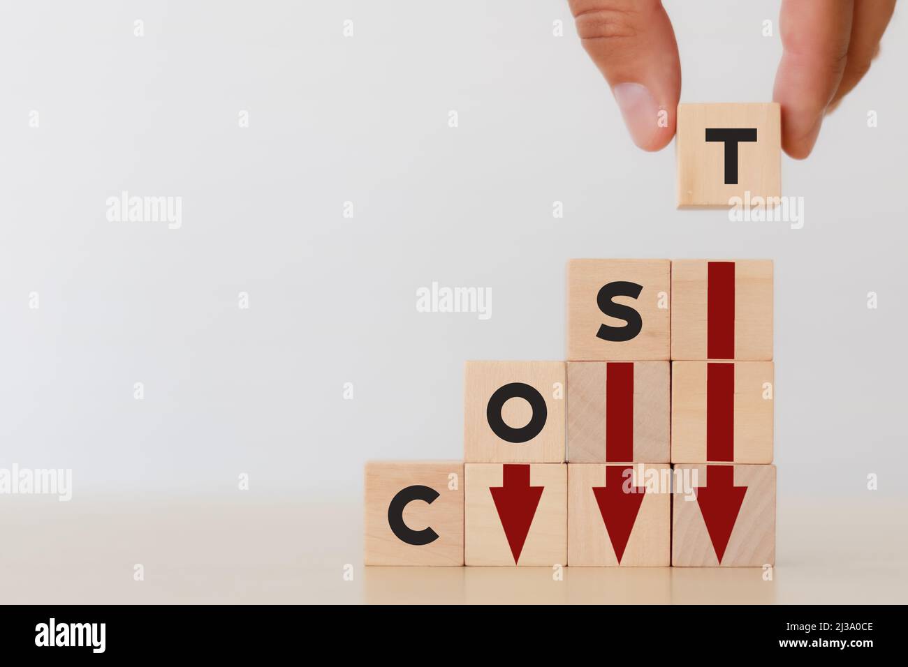 Concetto di riduzione dei costi. Gestione snella della produzione. Ridurre le spese aziendali per massimizzare i profitti. Mano mette il cubo di legno con il testo "costo" con il rosso Foto Stock