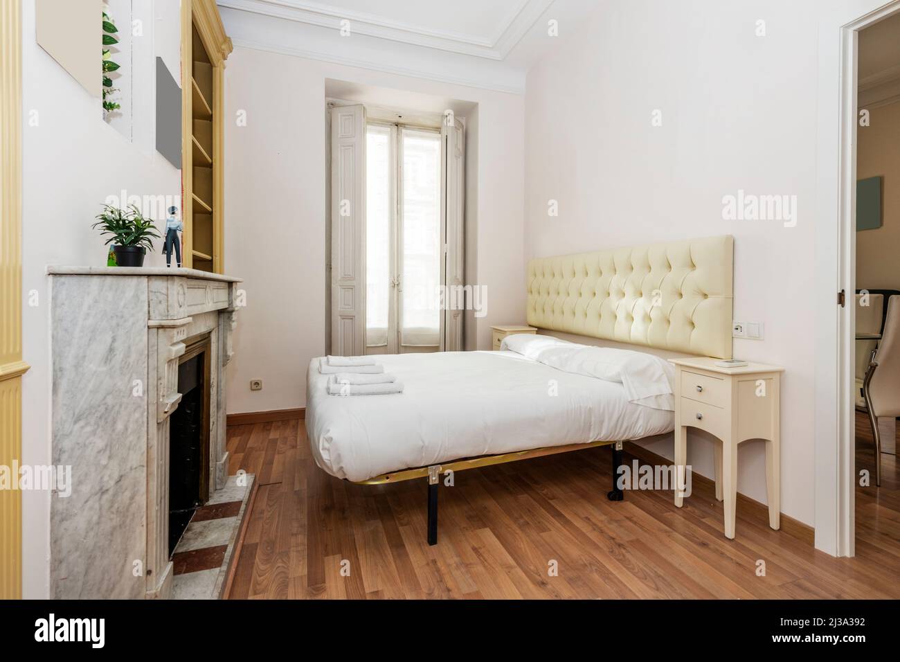 Camera da letto con letto matrimoniale con testiera color crema rivestita in stile capitone e caminetto in marmo bianco Foto Stock